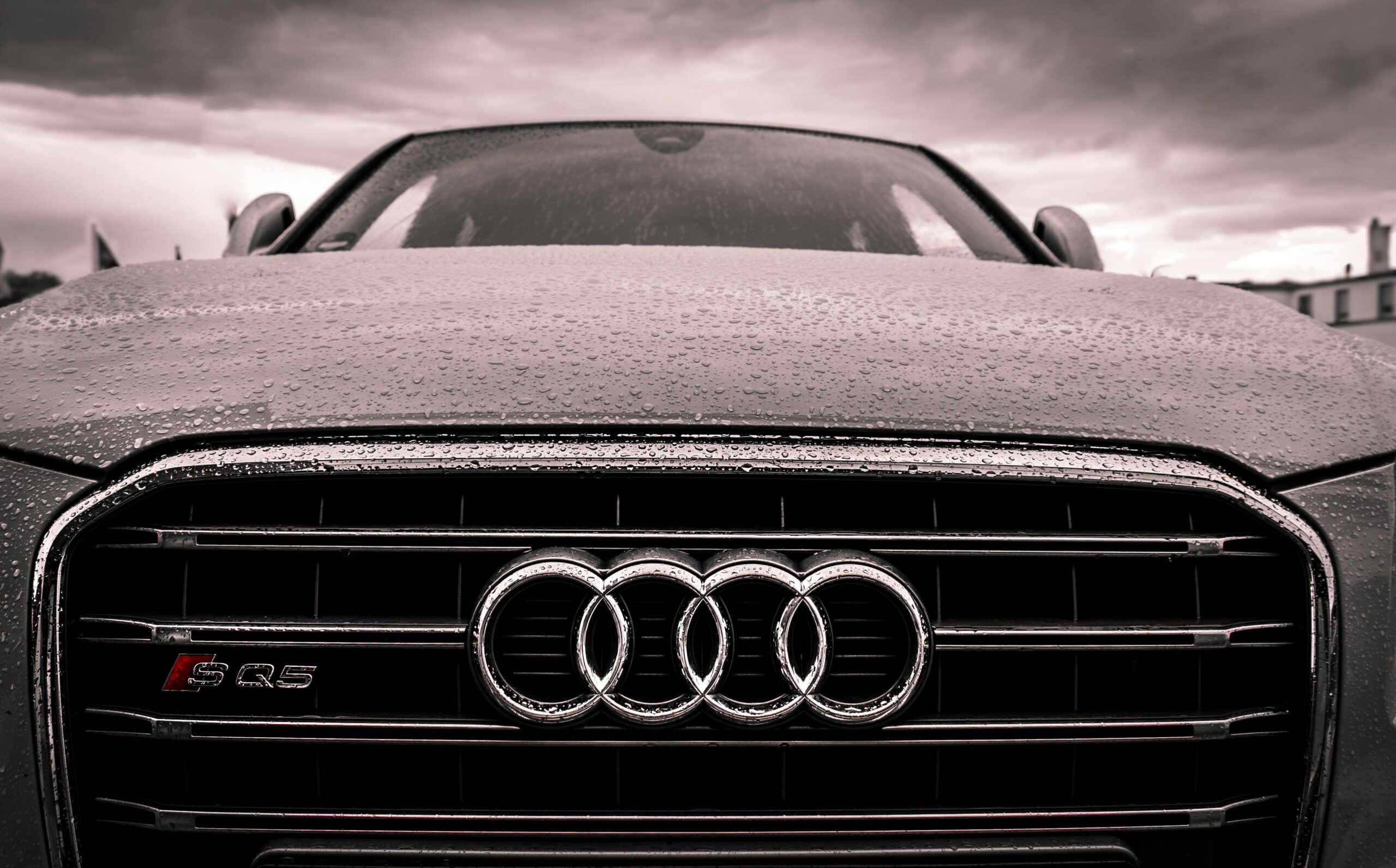Close-up of a rain-covered Audi car grille showcasing luxury and elegance under cloudy skies.
